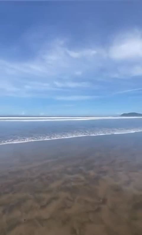 Playa Jacó at low tide: wet dark sand, long lines of white surf and a headland on the horizon.