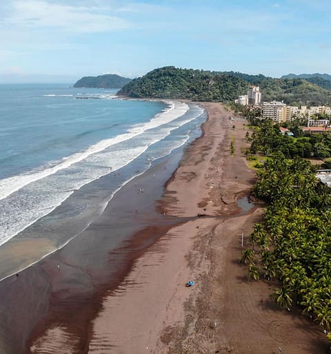Playa Jacó from above: dark sand, lines of surf and the hills at the end of the bay.