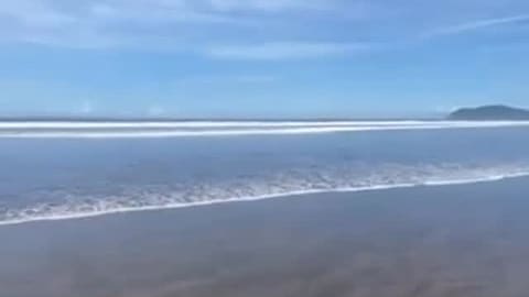 Wide view of Playa Jacó: long lines of whitewater under a big blue sky.