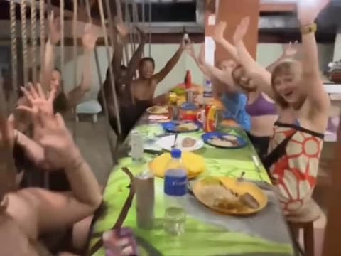 A shared dinner at the hostel: guests raise their hands around the hibiscus-painted table.
