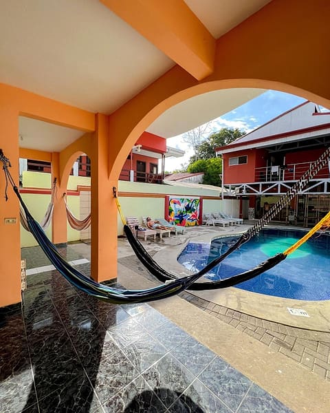 A hammock strung under an orange arch, the pool and red upstairs rooms beyond.