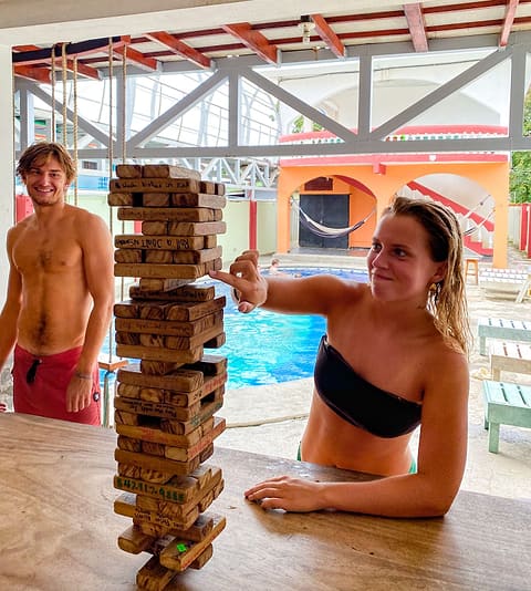 Two guests laughing over a tower of giant Jenga by the pool.