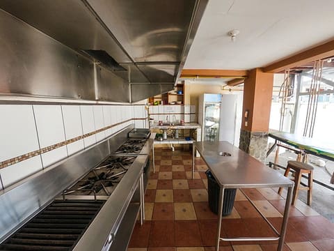 The community kitchen: long stainless-steel counters, a prep table and fridges under orange beams.