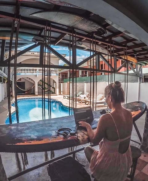 A guest working on a laptop at a table on the upstairs walkway, the pool below.