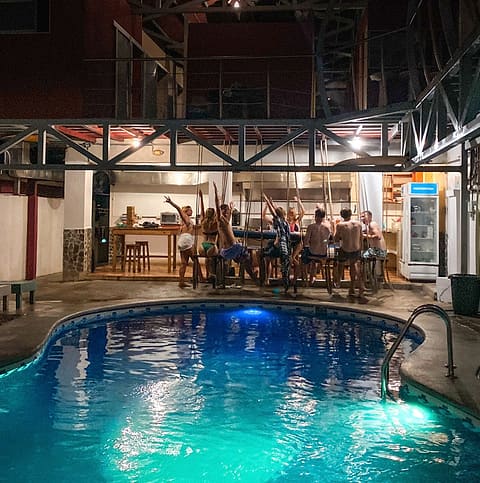 The pool glowing turquoise at night, with guests gathered at the tables behind it.