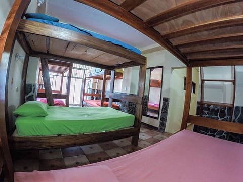 Dormitorio con camarotes de madera maciza, sábanas verdes y rosadas, piso de mosaico y un espejo.