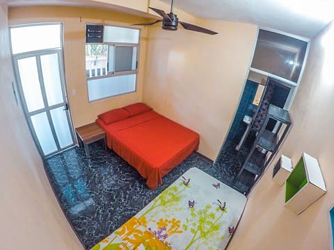Private room with a red double bed and a single bed with a flowered cover, ceiling fan and the ensuite door.
