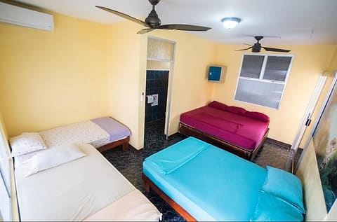 Habitación privada grupal con dos camas matrimoniales y dos individuales, dos abanicos de techo y un aire acondicionado de pared.