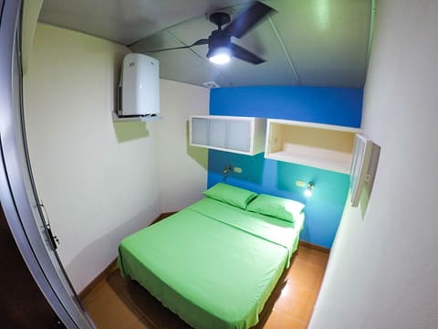 Small private room with a green double bed, a blue feature wall, a ceiling fan and a wall-mounted A/C unit.