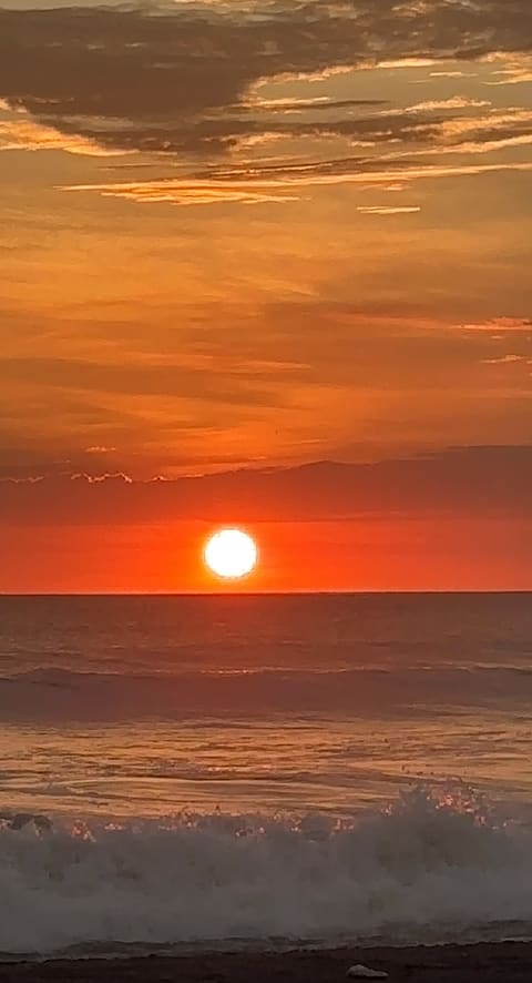 A fiery orange sun touching the Pacific horizon at Playa Jacó, waves breaking white in the foreground.