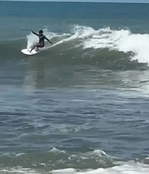 A surfer in a wetsuit carves along the face of a breaking wave at Jacó.