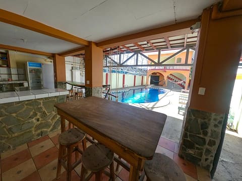 A high wooden table with stools under the arcade, looking out over the pool.